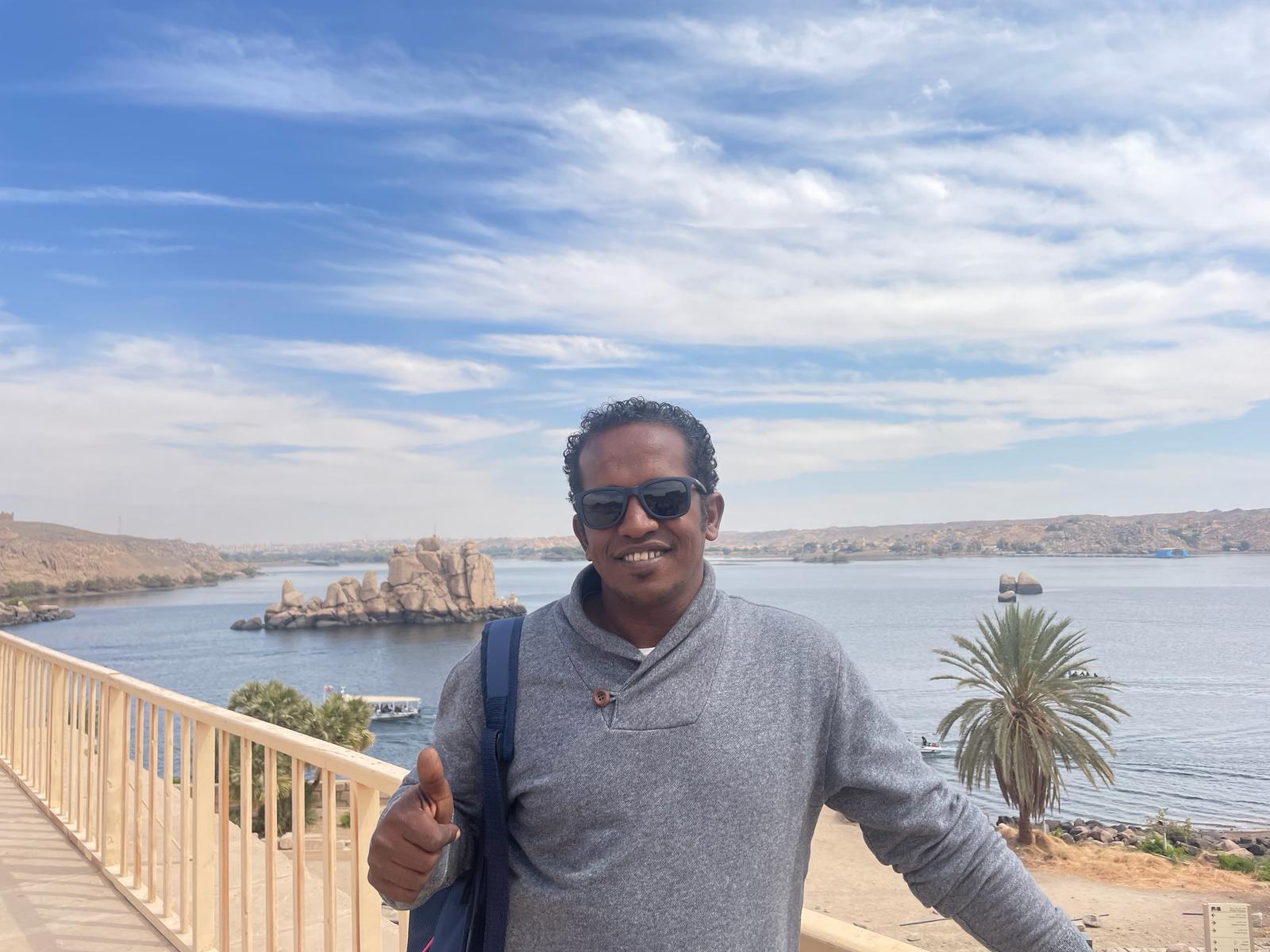 Mostafa Hashem - Professional Egypt Tour Guide at Aswan with Nile River and Ancient Granite Formations Background